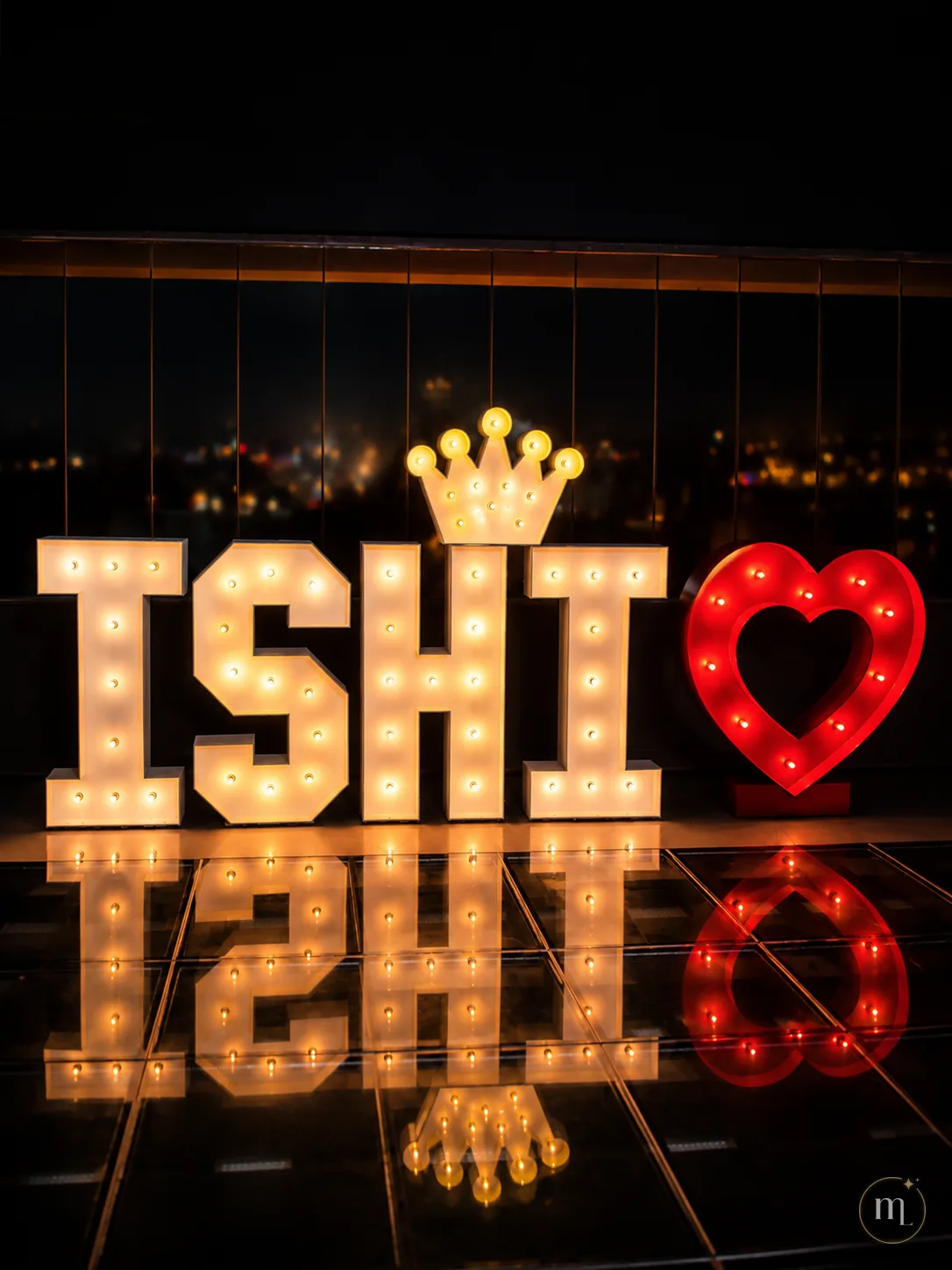 El nombre ISHI iluminado en una azotea de noche, con la corona y el corazón, reflejándose en el piso