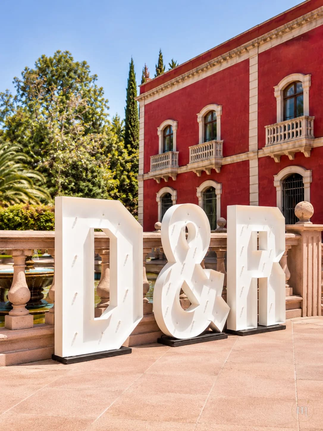 Las iniciales D y R con un ampersand, iluminadas frente a una hacienda de fachada roja