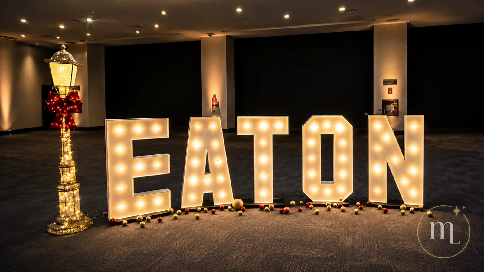 El nombre EATON en letras iluminadas dentro de un salón, junto a un farol y esferas doradas y rojas