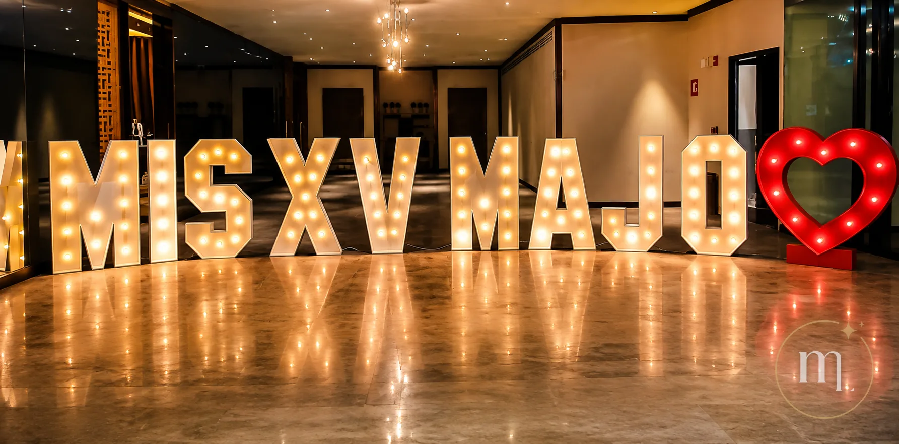 MIS XV MAJO en letras iluminadas con el corazón rojo al lado, reflejándose en el piso de mármol de un vestíbulo